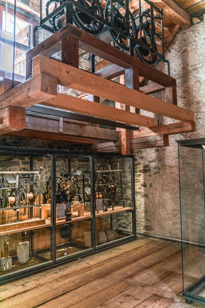Innenansicht des Zytturms der Museggmauer in Luzern mit historischem Uhrwerk hinter Glasvitrine, massiven Holzbalken und mittelalterlichem Natursteinmauerwerk