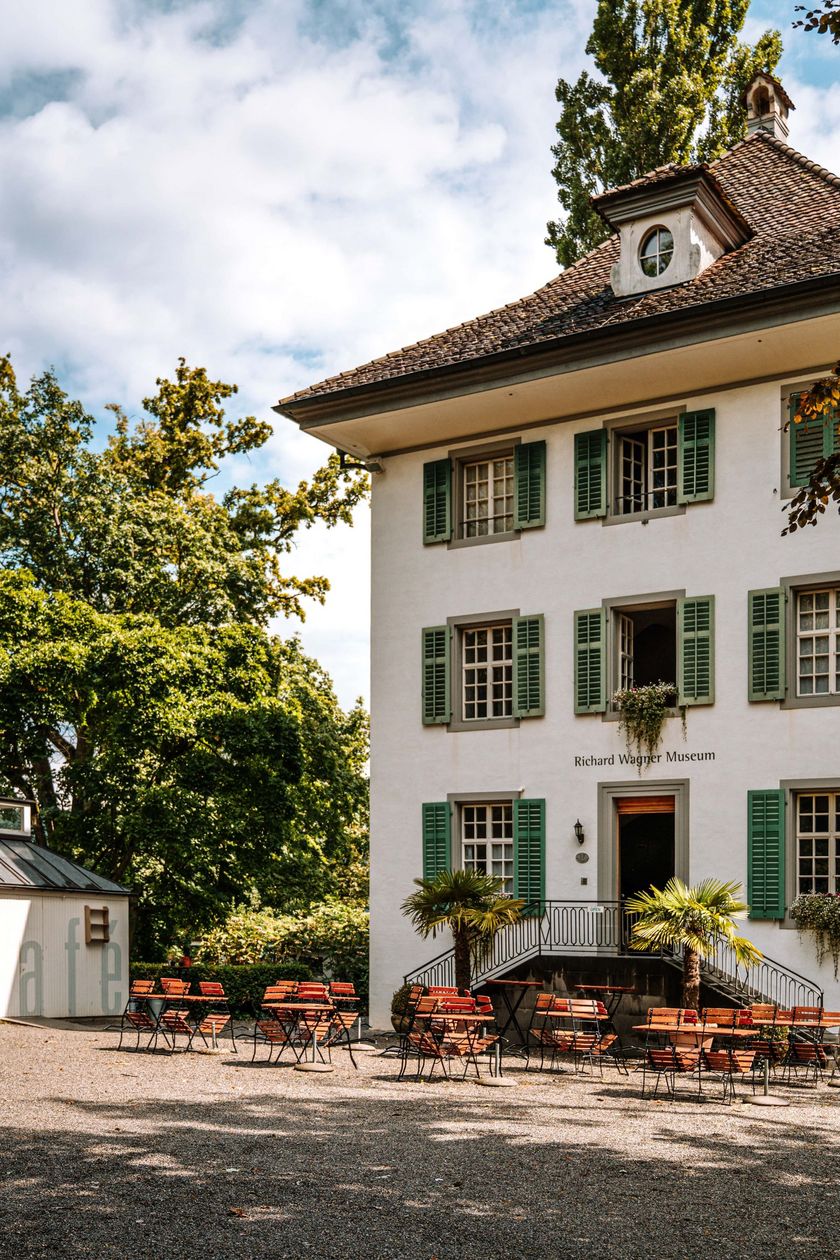 Weisses Haus mit grünen Fensterläden im Park, davor Tische und Stühle eines Cafés, Richard Wagner Museum in Luzern.