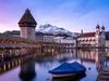 Winterliche Ansicht der Kapellbrücke mit Wasserturm in Luzern, im Hintergrund der Pilatus; fotografiert vom Rathausquai mit verschneiter Promenade im Vordergrund.