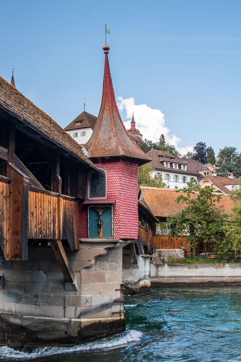 Gedeckte Holzbrücke Spreuerbrücke über die Reuss in Luzern mit dem roten Mühlenturm im Vordergrund und der Altstadt im Hintergrund, aufgenommen an einem sonnigen Sommertag.