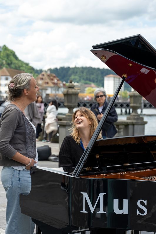 Menschen singen und spielen auf einem frei zugänglichen Open Piano in der Altstadt von Luzern bei sonnigem Wetter.