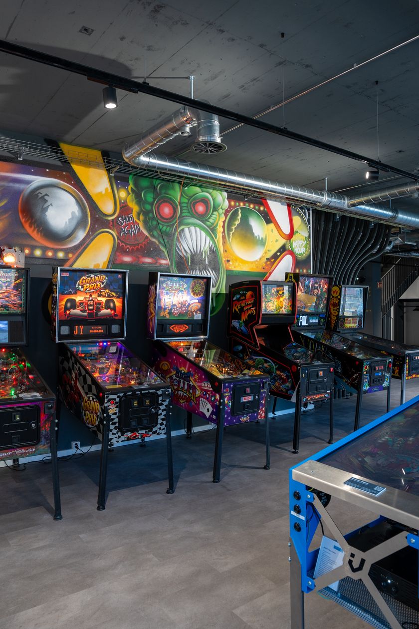 Innenraum des Gameorama in Luzern mit mehreren Flipperkästen und Arcade-Automaten vor einer bunten Graffiti-Wand.