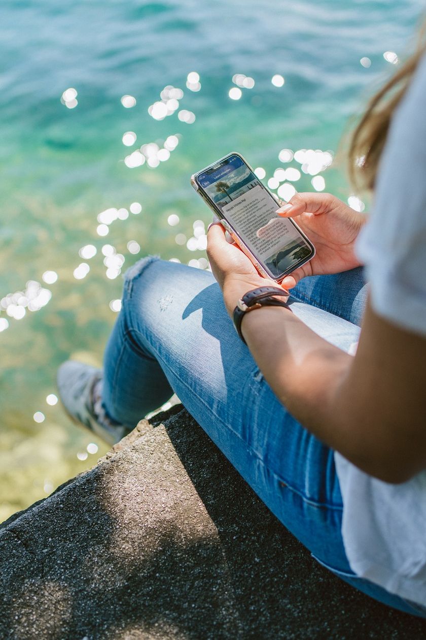 Frau sitzt am Ufer des Vierwaldstättersees und hält ein Smartphone mit der Luzern Audio-Guide-App in den Händen.