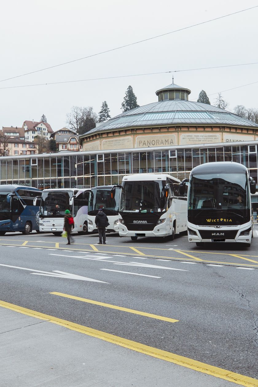 Mehrere Reisecars parken auf dem Carparkplatz am Löwenplatz in Luzern, im Hintergrund das Bourbaki Panorama.