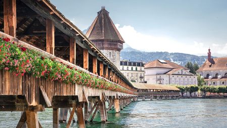 Kapellbrücke mit Wasserturm in Luzern bei Tag, geschmückt mit roten farbenfrohen Blumen.