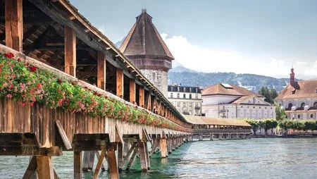 Kapellbrücke mit Wasserturm in Luzern bei Tag, geschmückt mit roten farbenfrohen Blumen.
