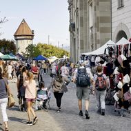 Menschen beim Schlendern über den Monatsmarkt in Luzern vor der Jesuitenkirche und Marktständen mit regionalen Produkten.