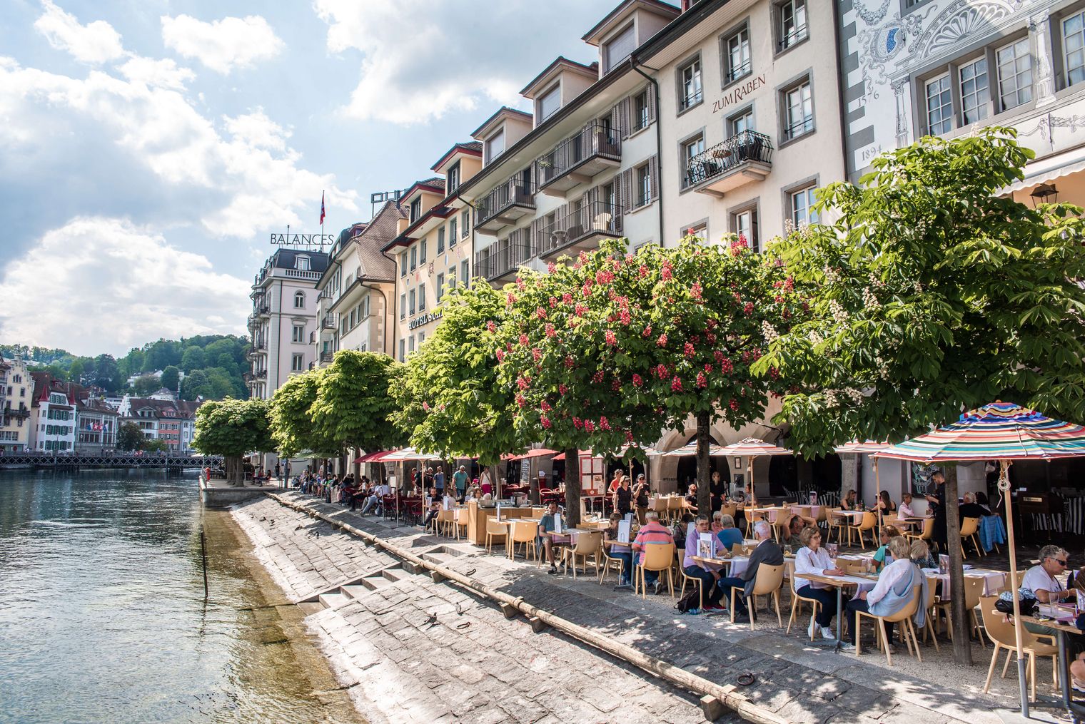 Sommerlicher Blick auf das Ufer bei der Unteren Egg in Luzern mit Spaziergängern entlang der Promenade und Sicht auf den See.
