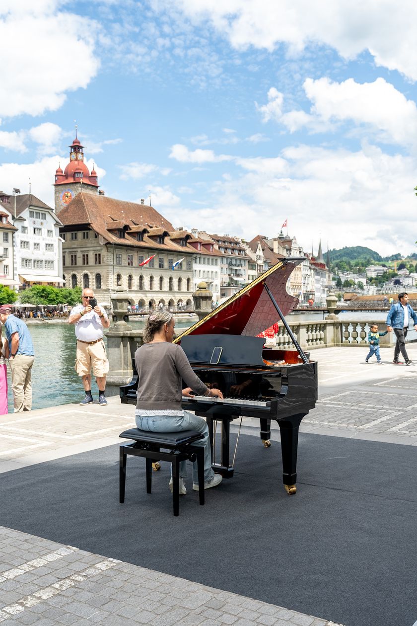 Menschen spielen auf einem frei zugänglichen Open Piano in der Altstadt von Luzern bei sonnigem Wetter.