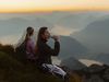 Zwei Wanderinnen machen auf dem Pilatus Pause und blicken im erwachenden Morgenlicht des Sonnenaufgangs auf das Bergpanorama der Zentralschweiz.