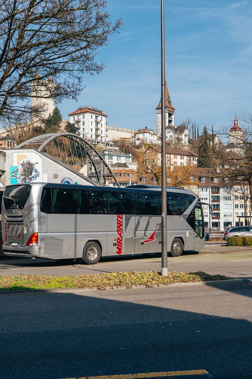 Zwei Reisecars stehen auf dem Kasernenplatz in Luzern. Im Hintergrund sind Altstadtgebäude, ein Kirchturm und eine Fussgängerbrücke zu sehen.